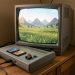 Console de jeu rétro grise avec cartouche colorée et manette à trois branches, reliée à un téléviseur cathodique affichant une paisible prairie fantastique en trois dimensions.