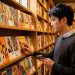 Un jeune homme découvre une sélection de bandes dessinées japonaises aux couvertures colorées dans une librairie chaleureuse.
